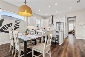 Una cocina moderna con armarios blancos, electrodomésticos de acero inoxidable y un comedor con mesa y sillas de madera.
