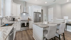 A modern kitchen with white cabinetry, stainless steel appliances, and a marble island.