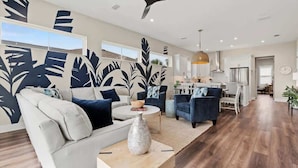 A modern living room with a sofa, armchairs, a coffee table, and a dining area with a chandelier.