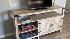 Et træ-TV-bord med et fladskærms-TV, en skål og farverige håndklæder.