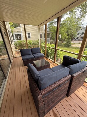 A covered outdoor seating area with wicker furniture and a glass enclosure. - Two if By Sea - Starboard Quarters (Rehoboth Beach)