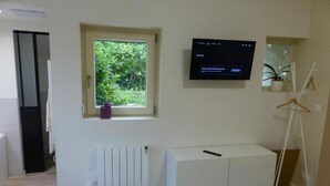 A room with a window, a radiator, a white cabinet, a television, and a plant. - Gîte de Charme : Les Charrons (Meursault)