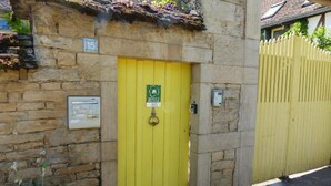 A stone building with a yellow door, a mailbox, and a number plate. - Gîte de Charme : Les Charrons (Meursault)