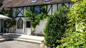 A traditional half-timbered building with a small garden area, a table and chairs, and a door with a window. - Gîte de Charme : Les Charrons (Meursault)