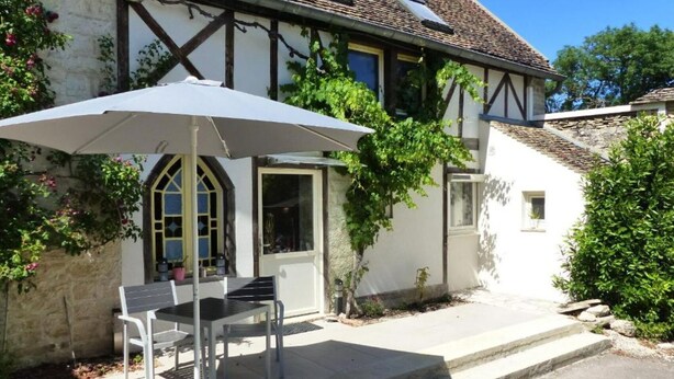 A traditional half-timbered house with a patio area featuring a table and chairs under a white umbrella. - Gîte de Charme : Les Charrons (Meursault)