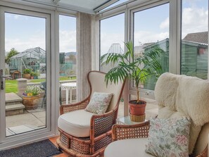 A conservatory with a wicker chair, a fluffy sofa, and a potted plant. - 2 bedroom accommodation in Ceres, near Cupar (Ceres, near Cupar)
