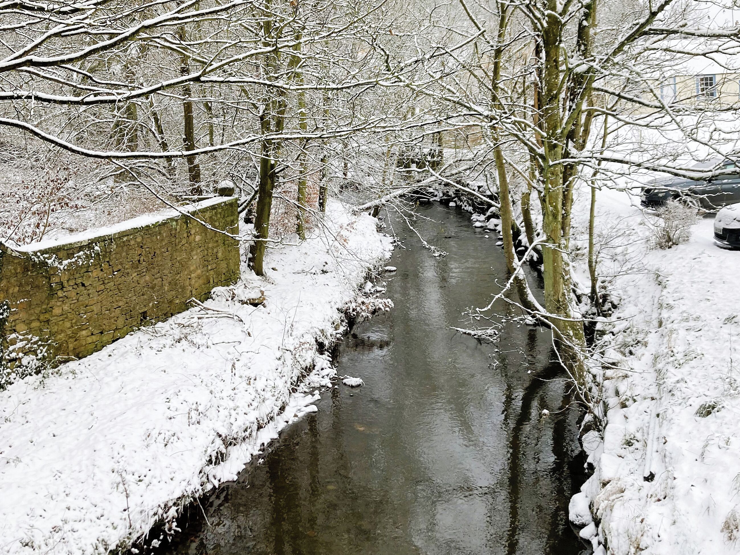 A narrow, snow-covered canal flanked by bare trees and a stone wall.