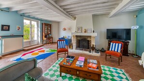 A living room with a fireplace, a television, and a coffee table with books. - Maison Prado - avec piscine privée et grand jardin (Magny-en-Vexin)