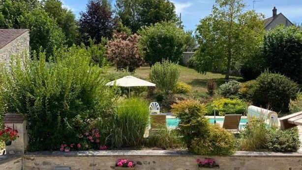 A wooden deck with a round table and chairs, surrounded by stone walls and potted plants. - Maison Prado - avec piscine privée et grand jardin (Magny-en-Vexin)