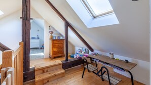 Habitación estilo loft con techo inclinado, escalera de madera, un escritorio con libros y material de escritura, y un tragaluz.