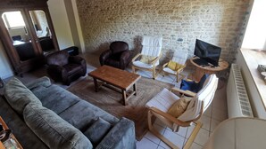 Una sala de estar acogedora con pared de piedra, vigas de madera en el techo, sillones de cuero, un sofá y un televisor sobre una mesa de madera.