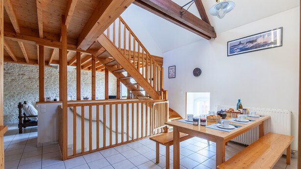 Una habitación amplia con una escalera de madera, una mesa de comedor con platos y tazas, y un banco.
