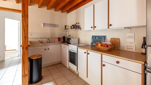 Una cocina con armarios blancos, vigas de madera, microondas, estufa y cubo de basura.