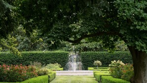 Un giardino formale con una fontana al centro, siepi curate e una varietà di piante fiorite.