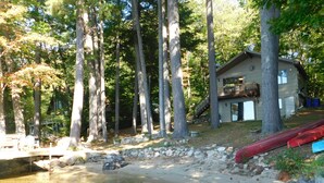 A cabin with a dock, surrounded by tall trees and a small pond. - Peaceful Long Lake Escape – Dock, Kayaks, & Seasonal Charm (Naples)