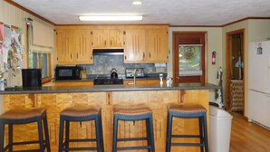 A kitchen with wooden cabinets, a microwave, a toaster, and a coffee maker. There are three stools at the counter. - Peaceful Long Lake Escape – Dock, Kayaks, & Seasonal Charm (Naples)
