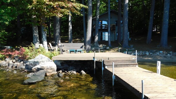 A wooden dock extending into a clear stream, surrounded by rocks and trees. - Peaceful Long Lake Escape – Dock, Kayaks, & Seasonal Charm (Naples)