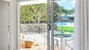 Una habitación moderna con puerta de vidrio que da a un patio. La habitación tiene ventilador de techo, una mesa redonda con cesta y una pequeña planta en maceta.