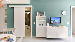 Un baño moderno con un tocador blanco, un televisor montado y un reloj en la pared.