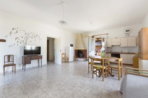 A spacious living area with a flat-screen TV, wooden furniture, a dining table, and a kitchen with cabinets and a stove. - 3326 Villetta Jannara by Barbarhouse (Melendugno)