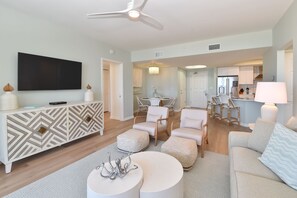 A modern living room with a flat-screen TV, white sofas, a patterned coffee table, and a dining area with chairs and a chandelier. - Beautifully Updated 9th Floor in Silver Shells St. Lucia! (Destin)