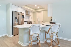 A modern kitchen with stainless steel appliances, a central island with bar stools, and light-colored cabinetry.