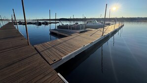 En træbrygge, der strækker sig ud i roligt vand, med både fortøjet i enden.