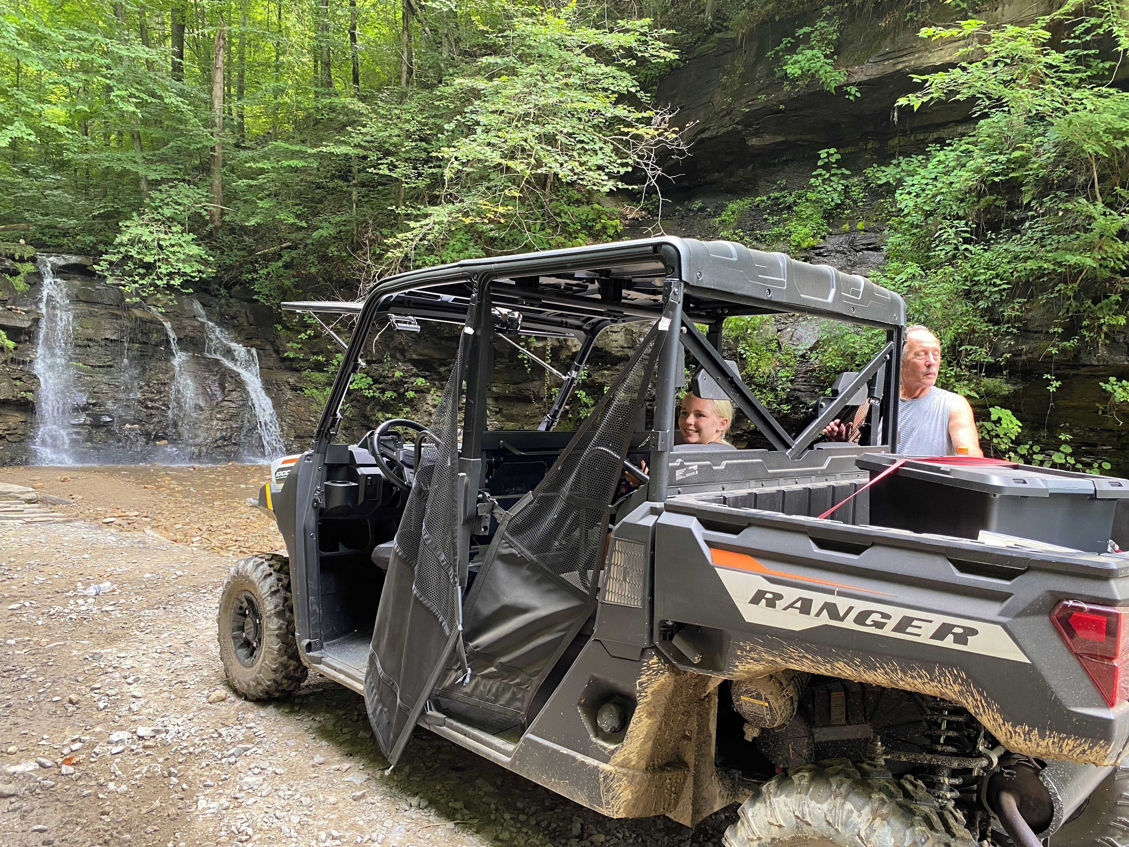 A Ranger vehicle parked near a waterfall in a forested area.