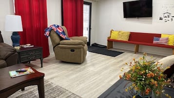 A living room with a brown sofa, a red couch, a TV mounted on the wall, and a wooden coffee table.