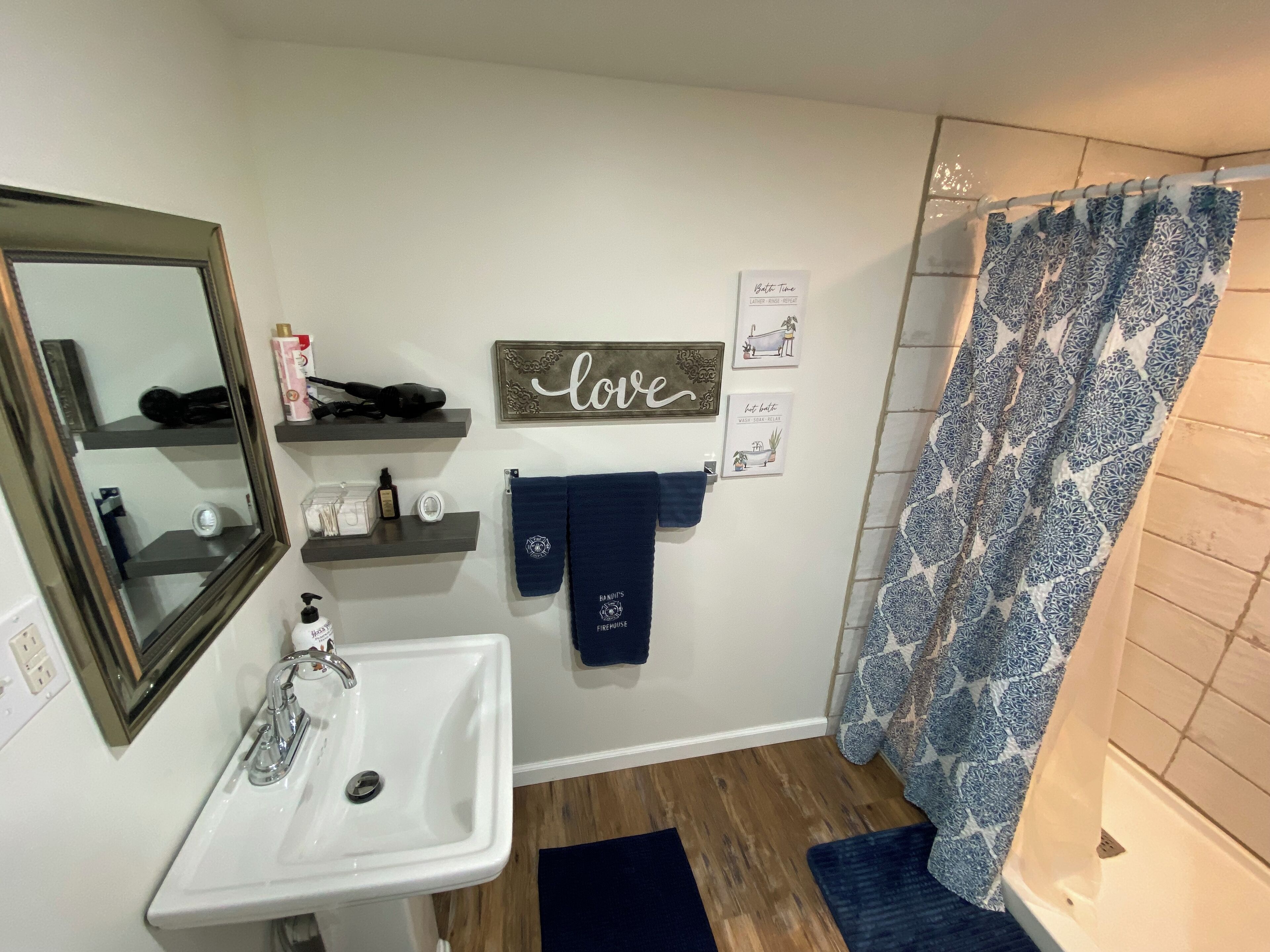 Un baño con un lavabo blanco, un espejo, toallero con toalla, cortina de ducha y estante con artículos de aseo.