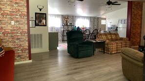 A living room with a brick wall, a green armchair, a plaid sofa, and a red armchair. - Firehouse Bandits Houses (Accoville)