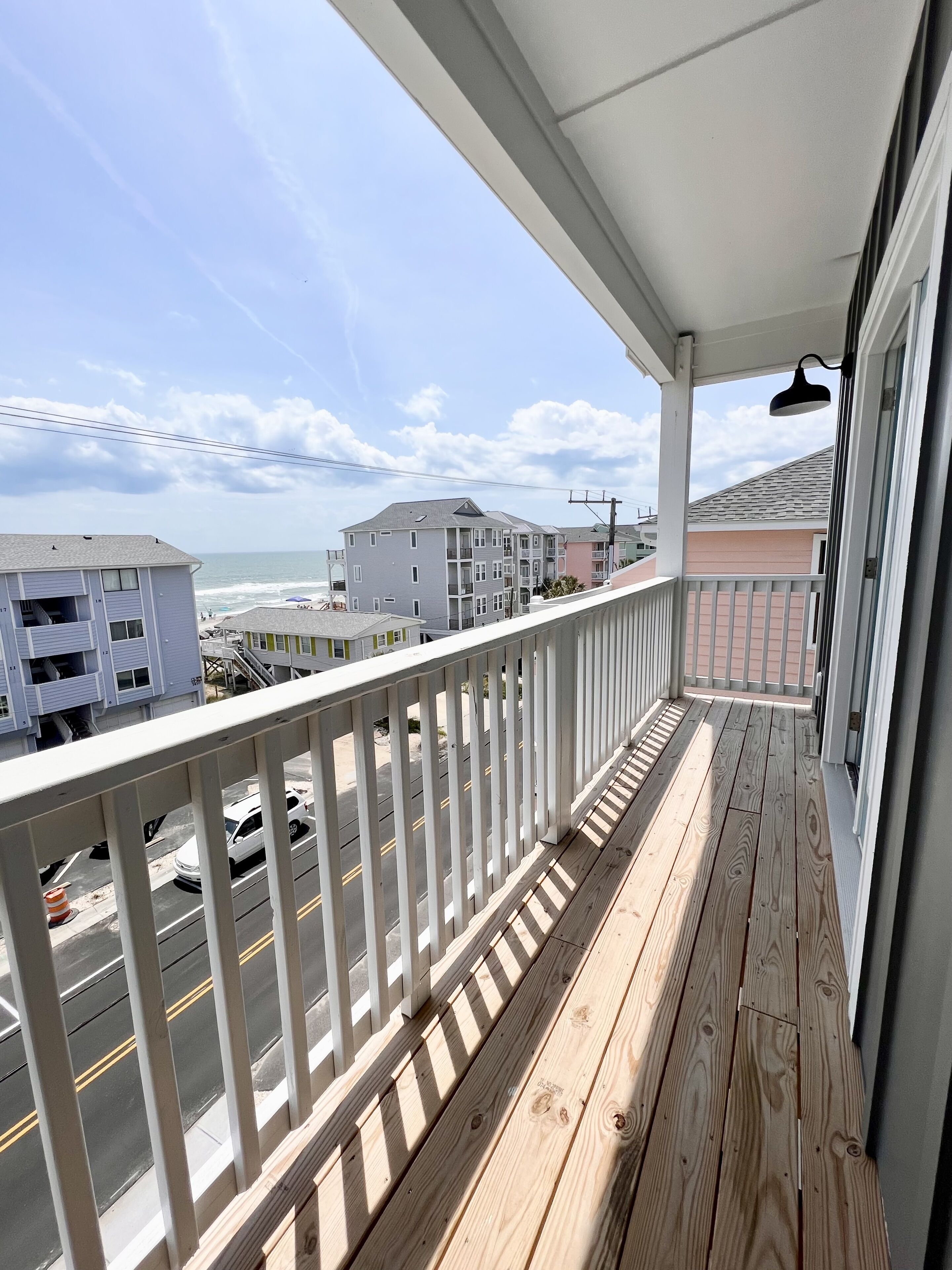 A wooden balcony with a white railing overlooking a street and buildings.