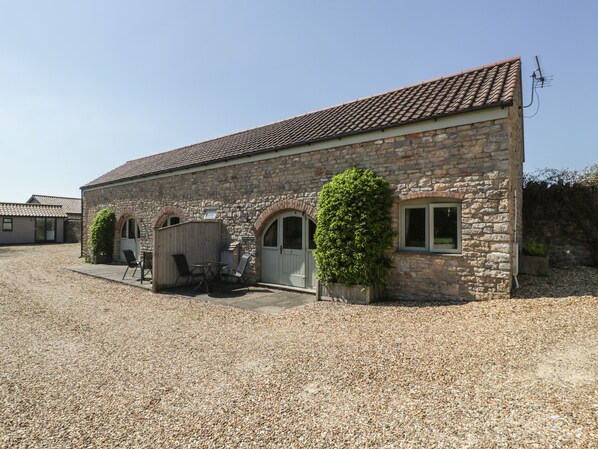 A stone building with a tiled roof, a gravel driveway, and a small patio with chairs. - Sunnyside (Weston-super-Mare)