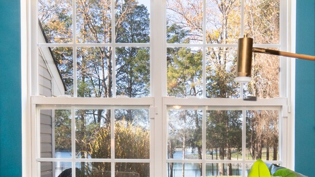 A room with a large window, a sofa, a side table with a book, and a potted plant.