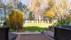 A patio with wicker furniture overlooking a grassy area with trees and a body of water.