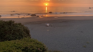 A beach with a sunset, rocks, and a person walking. - Oceanfront Cabin 4 with Private Jacuzzi & Stunning Views (Smith River)