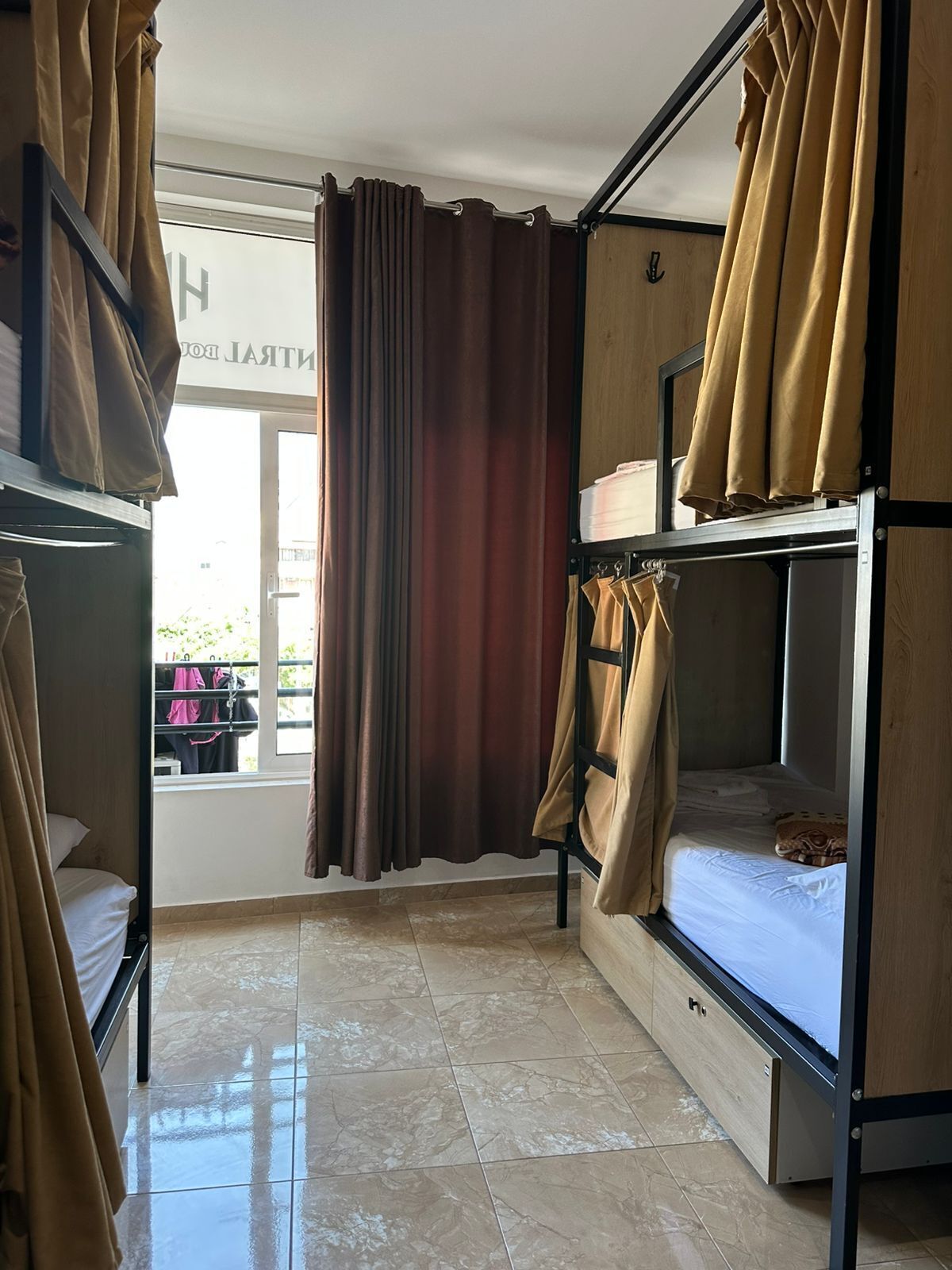 Una habitació amb llits superposats, una finestra amb cortines i un terra de rajoles.