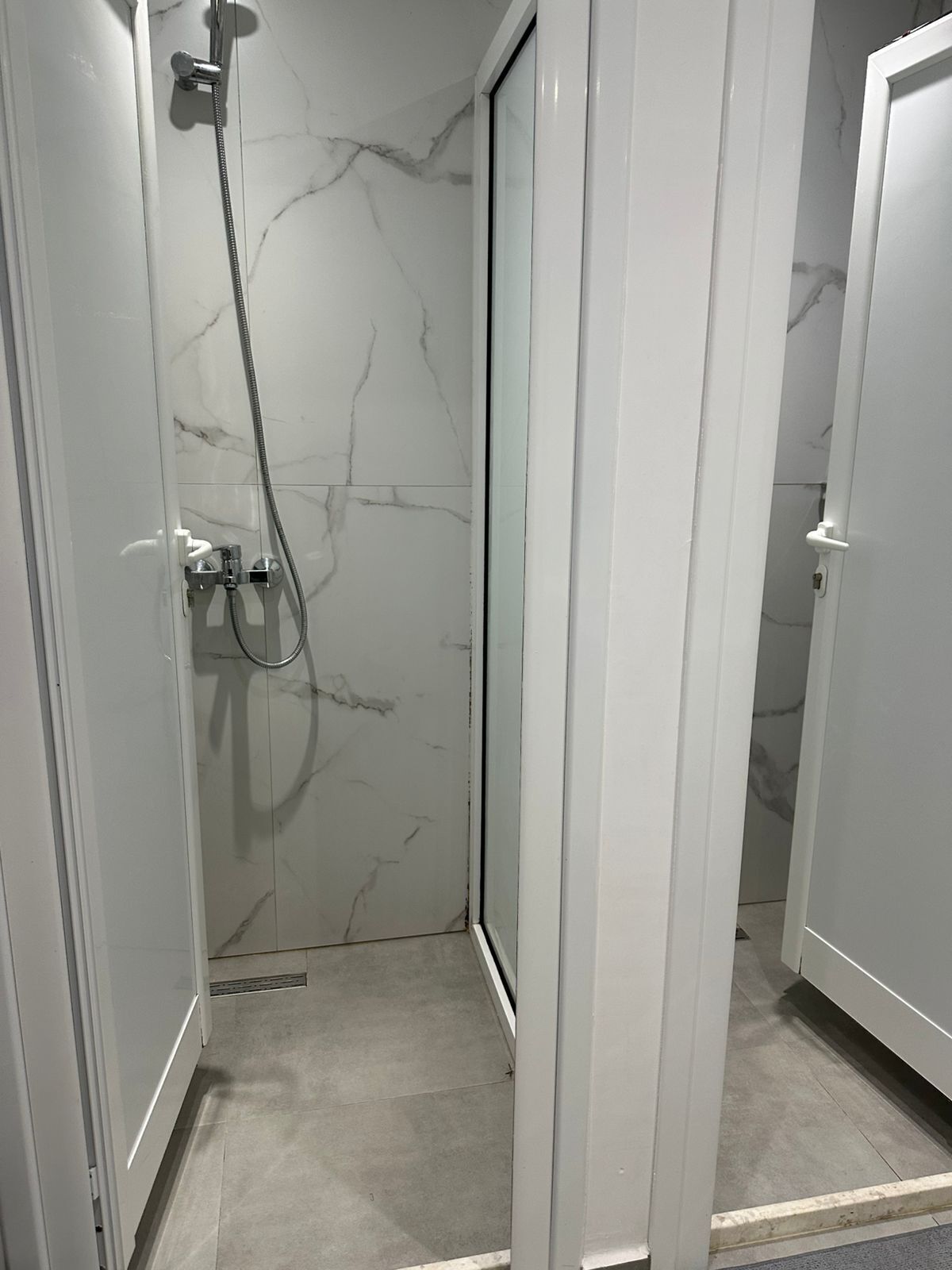 A walk-in shower with a marble wall, a showerhead, and a handheld shower attachment.