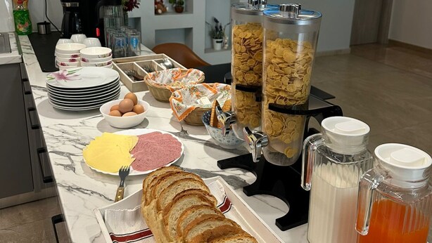 A breakfast buffet setup with various food items, a coffee machine, and a TV in the background.