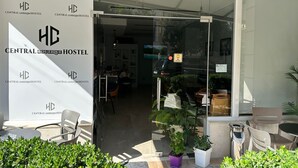 The entrance to Central Boutique Hostel with a glass door, outdoor seating area, and potted plants.