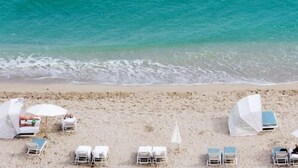 Una playa con sillas de playa blancas y sombrillas dispuestas sobre la arena.