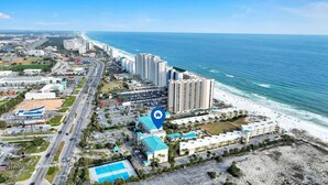 Um hotel à beira-mar com vários edifícios altos, um estacionamento e uma praia.