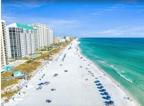 A beach with a row of high-rise buildings, clear blue water, and numerous umbrellas. - Quiet Destin Beachfront Resort! (Destin)