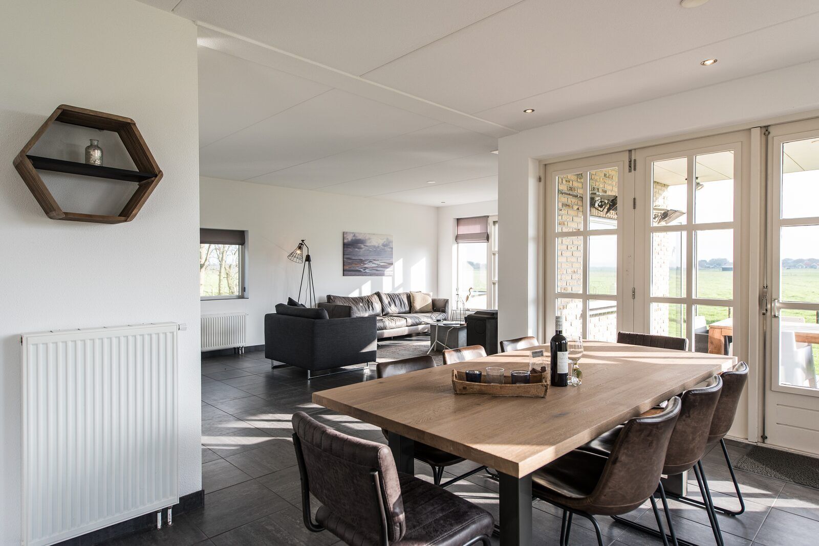 Un vaste espace de vie comprenant une grande table à manger en bois, des sièges confortables et une vue sur l’extérieur grâce à de grandes fenêtres.
