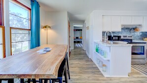 A modern kitchen with white cabinets, a wooden dining table, and a view of the backyard through a large window. - Whitehall Cottages (Whitehall)