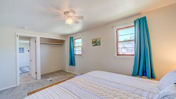 A bedroom with a bed, a ceiling fan, a window with curtains, and a closet.