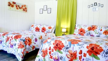 Habitación de hotel con dos camas, cubrecamas estampados con motivos florales, una cortina verde y un cuadro con fotografías en la pared.