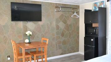 A room with a stone-patterned wall, a flat-screen TV mounted above a wooden table with chairs, a black refrigerator, and a microwave.