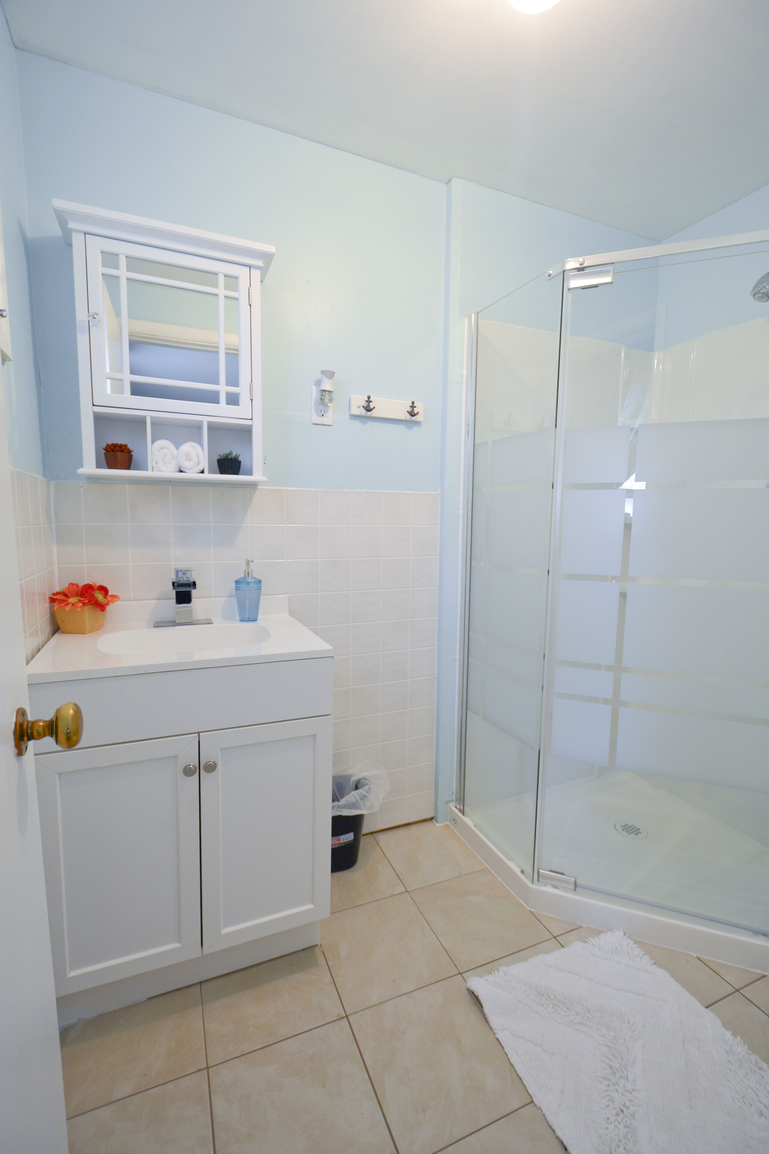 A bathroom with a white sink, a glass shower enclosure, and a white towel on the floor.