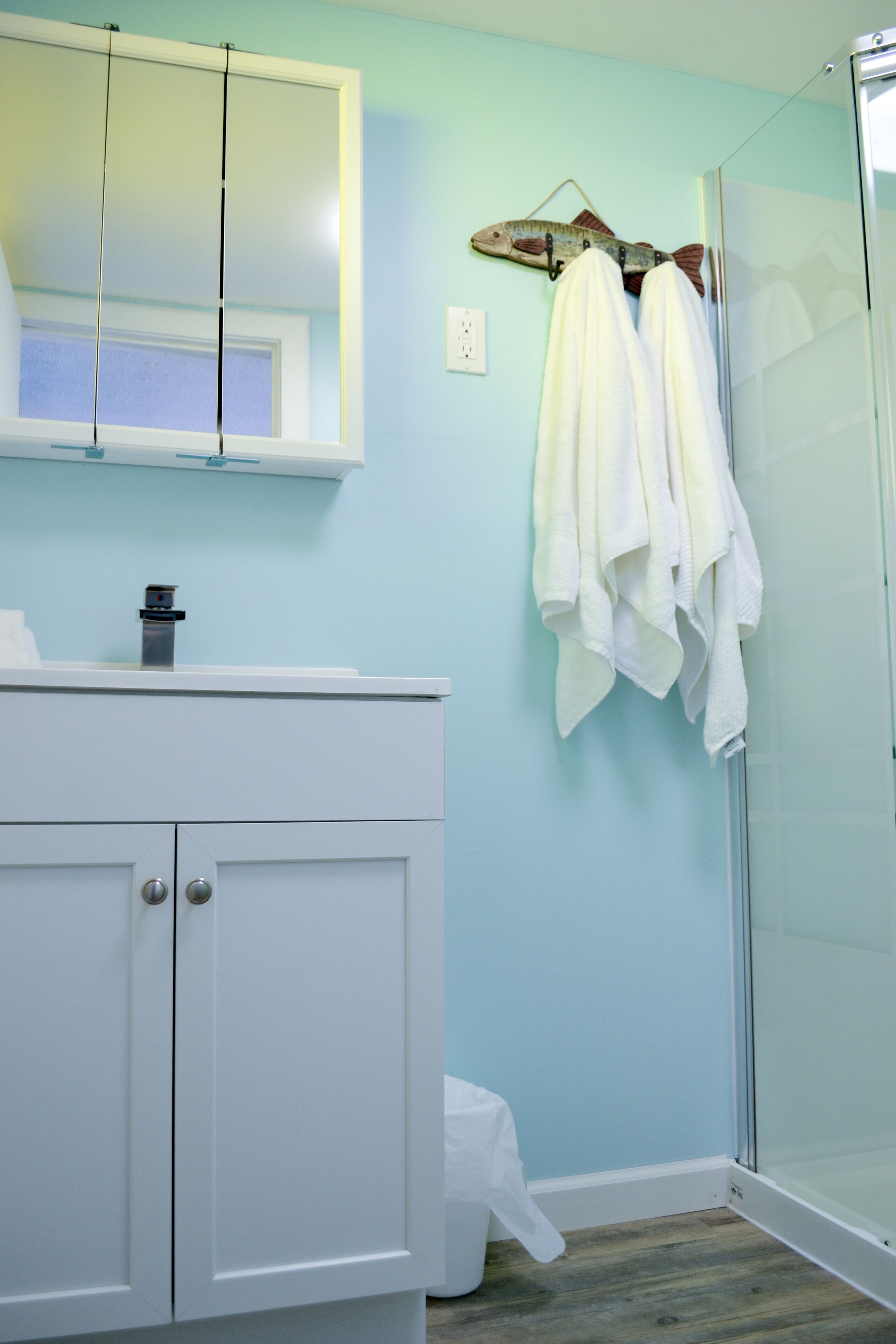 Une salle de bain avec un meuble-lavabo blanc, une cabine de douche en verre et un porte-serviettes avec des serviettes blanches.